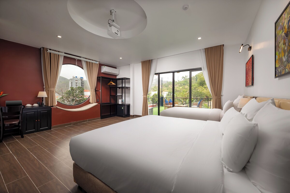 Une chambre d’hôtel avec un grand lit, un bureau, une chaise et une vue sur la verdure par la fenêtre.