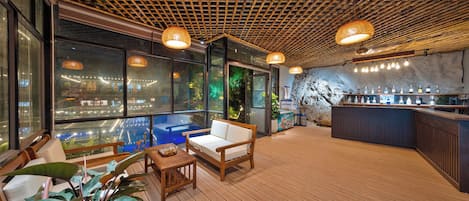 Uma área de bar moderna com piso de madeira, assentos e balcão com diversos tipos de garrafas.