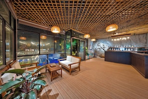 A modern bar area with a wooden floor, seating, and a bar counter with various bottles. - Cat Ba Sena Valley Retreat (Hai Phong)