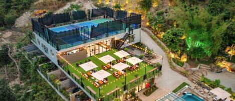 A multi-level resort with a pool, outdoor seating, and a tennis court.