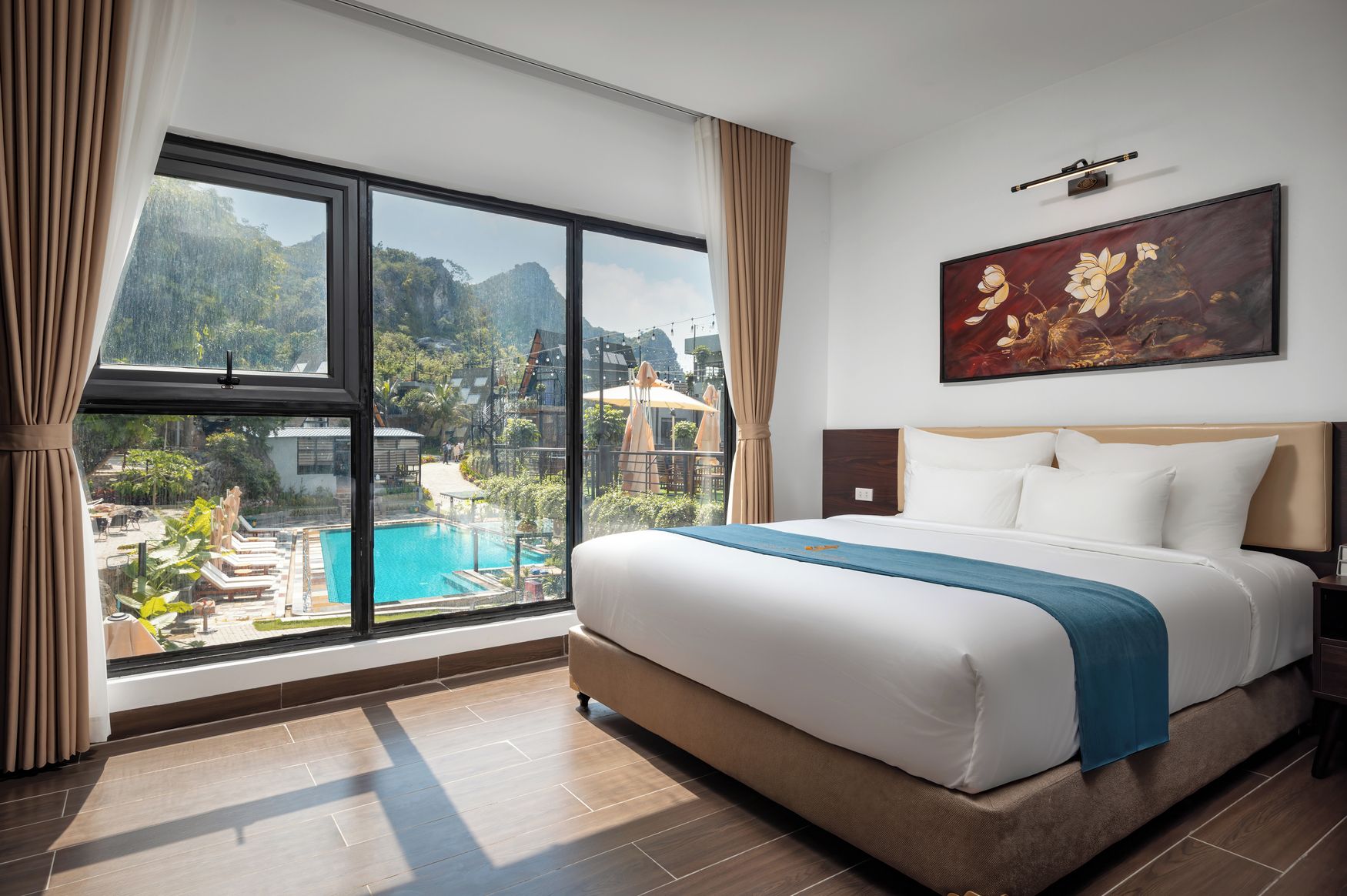 A hotel room with a large window, a bed, a painting, and a view of a pool and mountains.