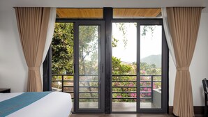 Une chambre avec un lit, une porte-fenêtre coulissante donnant sur un balcon et une vue sur la verdure.