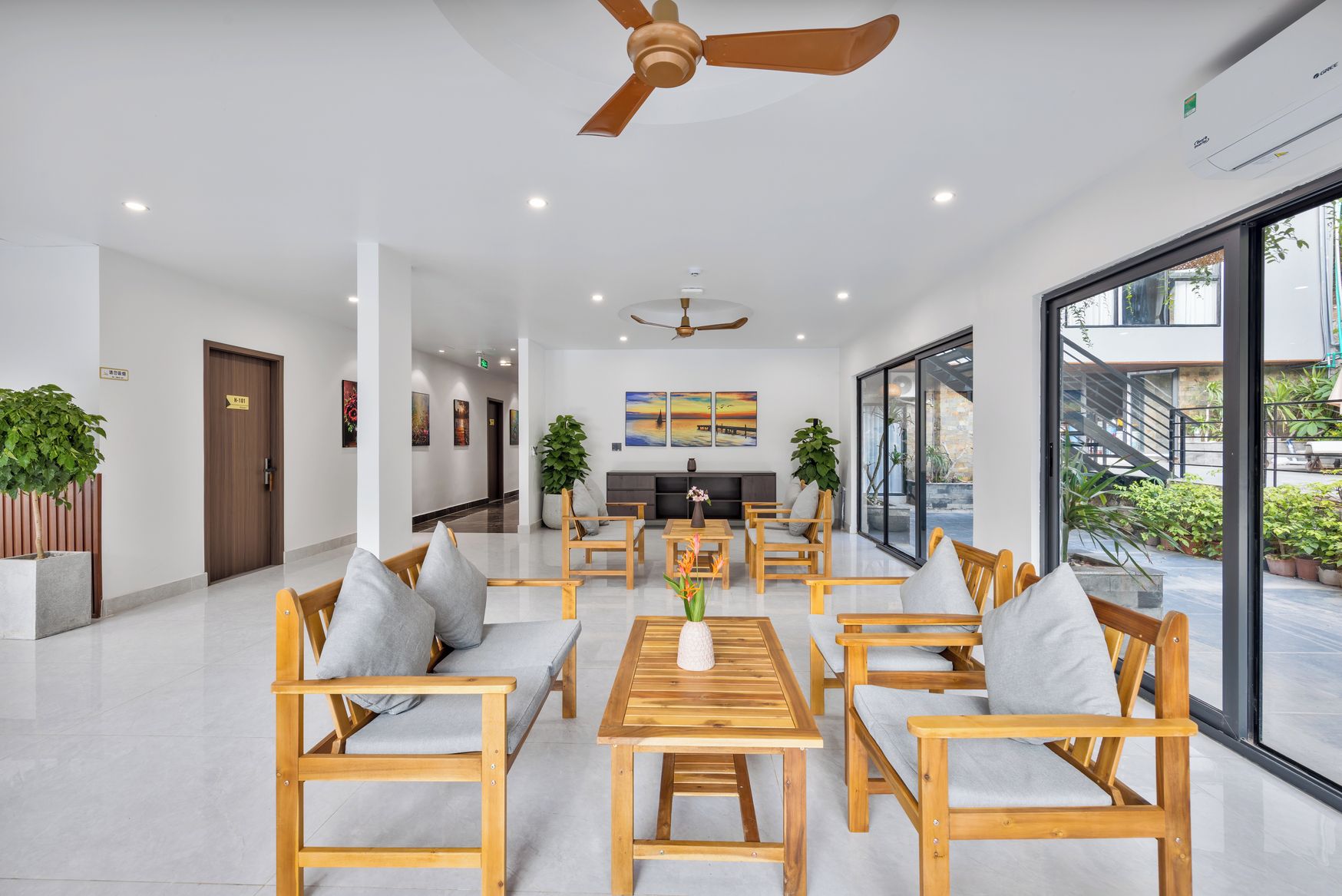 A spacious lobby with wooden furniture, a ceiling fan, and large windows offering a view of the outdoors.
