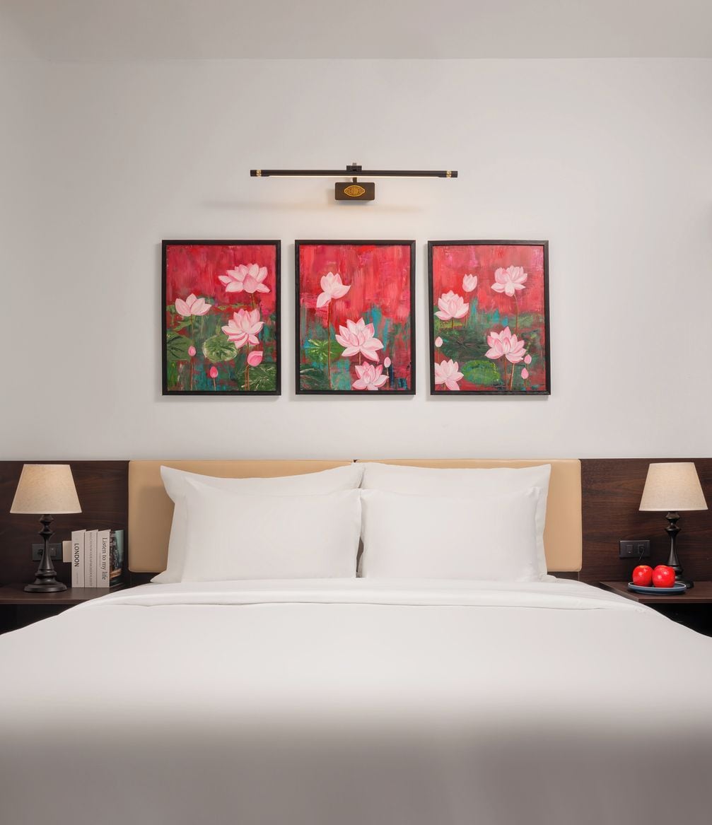 Une chambre d’hôtel avec un lit, deux tables de chevet et trois tableaux représentant des fleurs roses, accrochés au mur.
