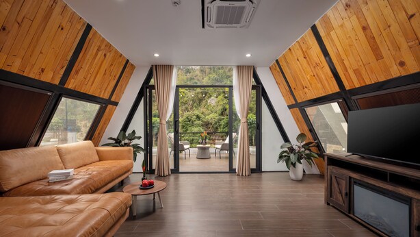 A modern living room with a leather sofa, a television, and a view of the outdoors. - Cat Ba Sena Valley Retreat (Hai Phong)