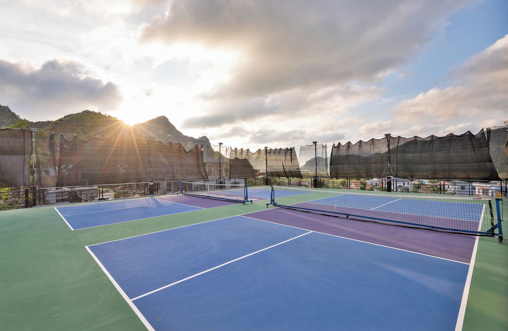 Un campo da tennis con rete, circondato da una recinzione, con montagne sullo sfondo.