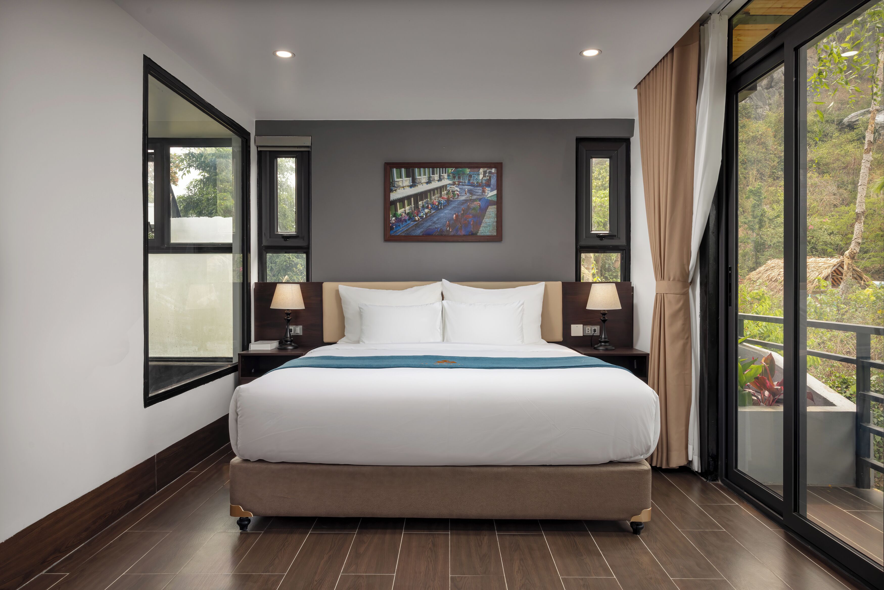 Een moderne hotelkamer met een groot bed, twee nachtkastjes met lampen, een schilderij aan de muur en een balkon met uitzicht.