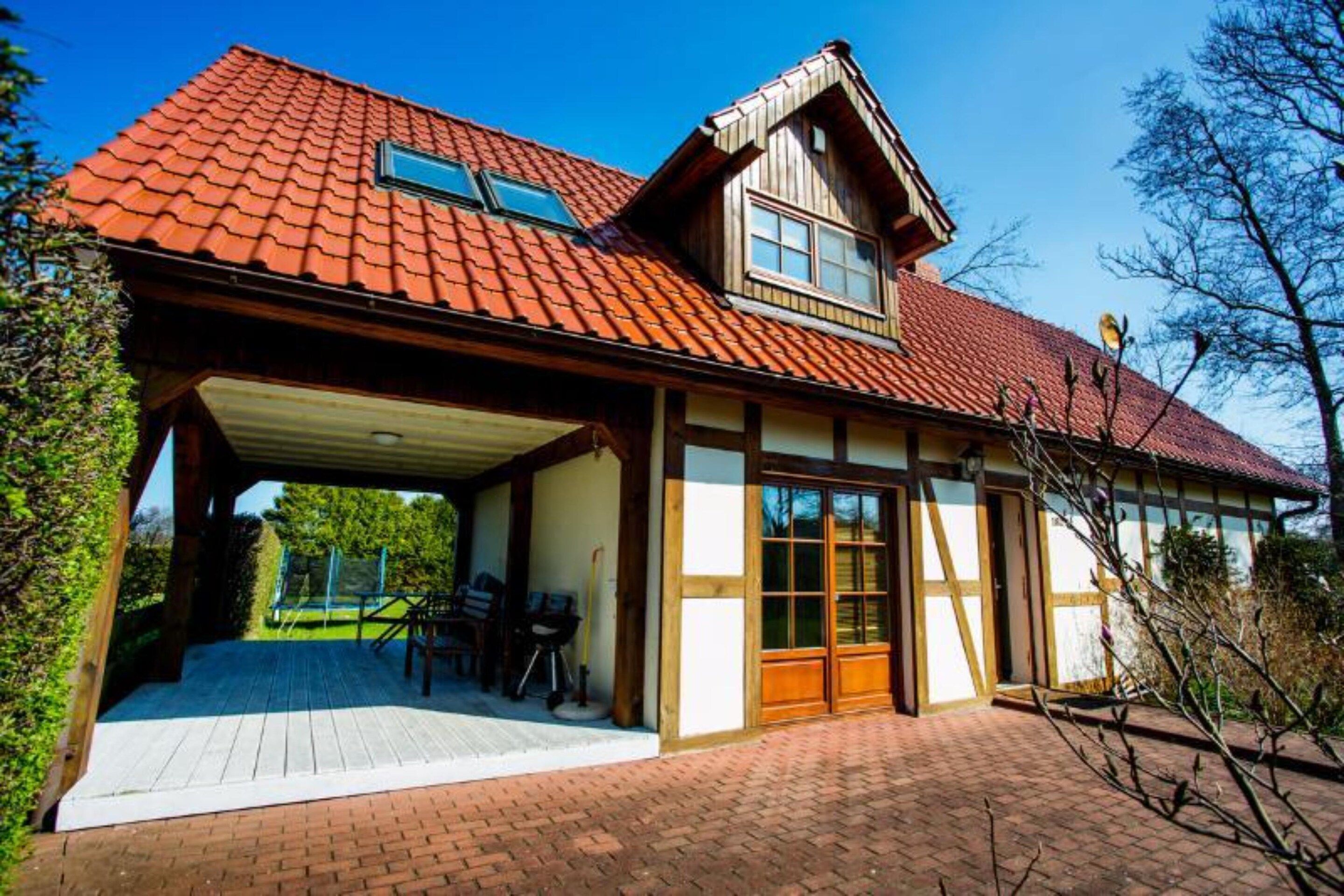 A house with a red tiled roof, a covered patio with a table and chairs, and a large window.