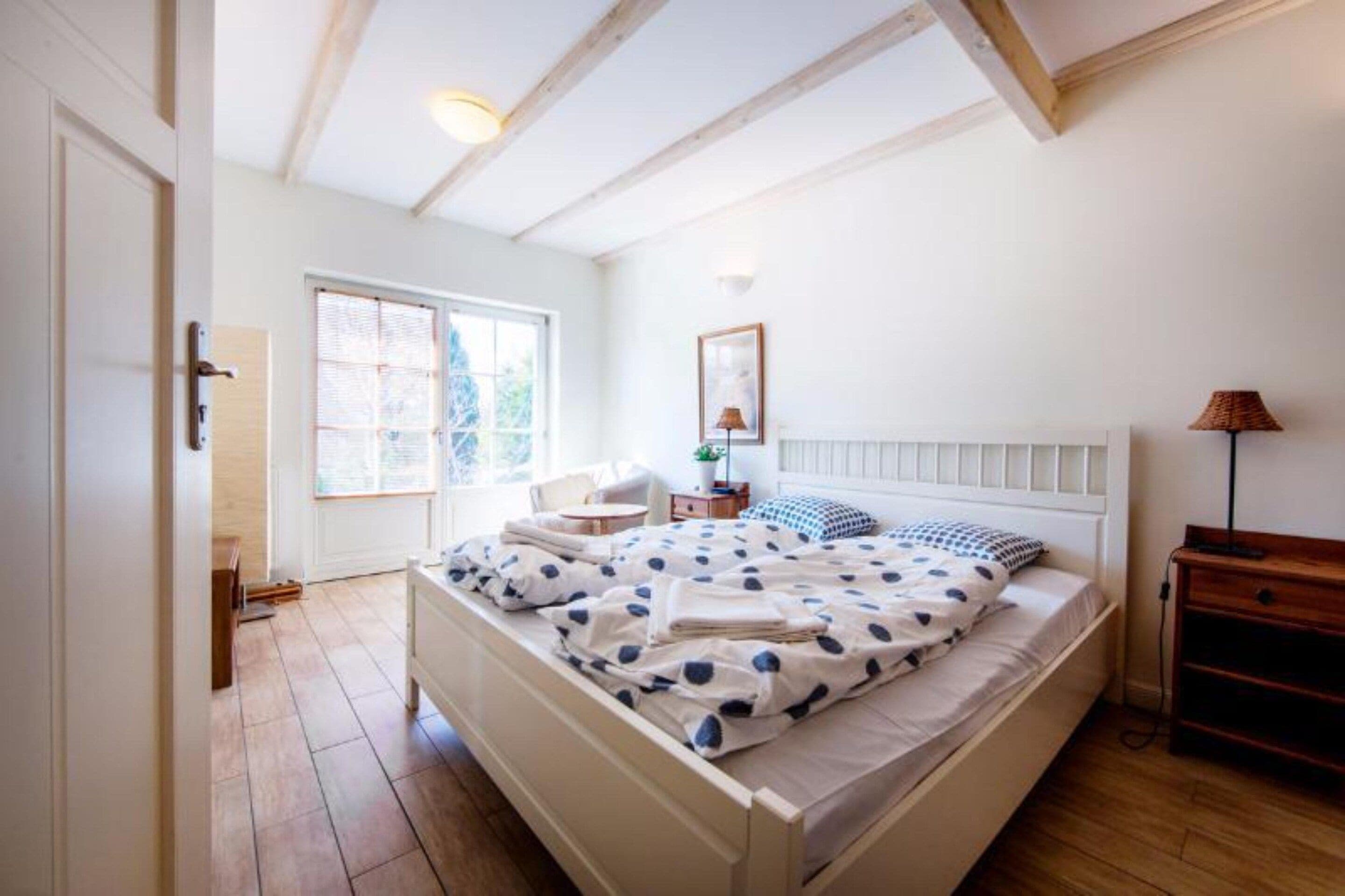 Un dormitorio con cama, mesita de noche, lámpara y ventana.