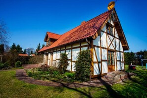 Une maison traditionnelle à ossature bois, avec un toit à pente recouvert de tuiles rouges et une antenne parabolique.
