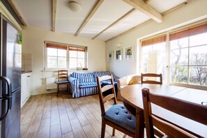 Un coin repas avec une table et des chaises en bois, un canapé à rayures et une fenêtre avec des stores.