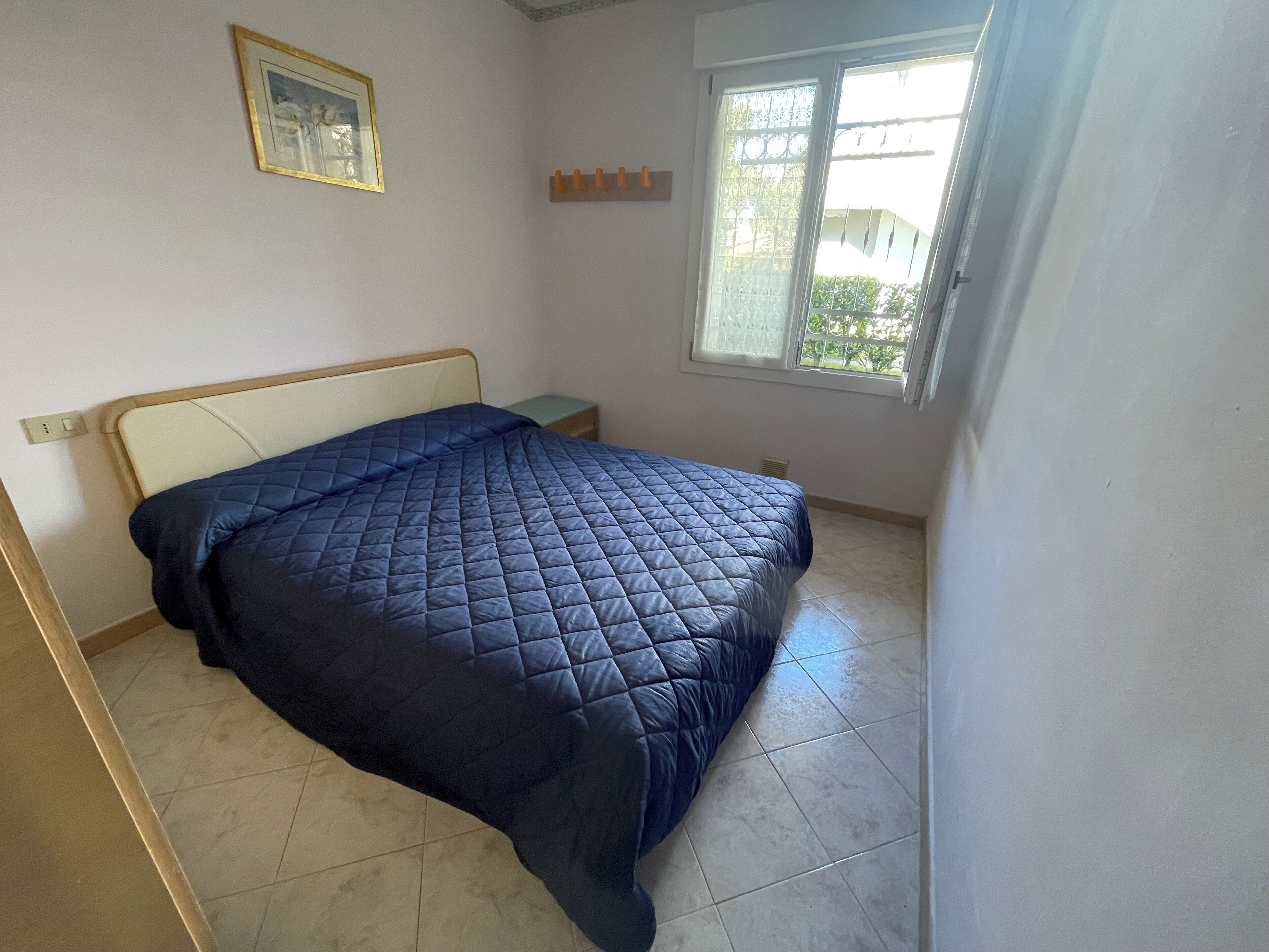 Ein Schlafzimmer mit Bett, Nachttisch, Fenster mit Blick und einem Wandbild.