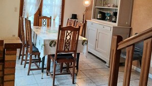 A dining area with a wooden table and chairs, a chandelier, and a cabinet with kitchen items.