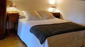 A bedroom with a sloped ceiling, wooden headboard, two bedside tables with lamps, a bed with white linens, and a dark throw blanket.