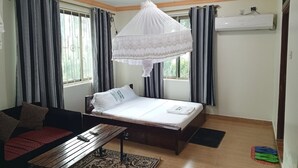 Een slaapkamer met een bed, nachtkastje, een hangend klamboe en een raam met gordijnen.