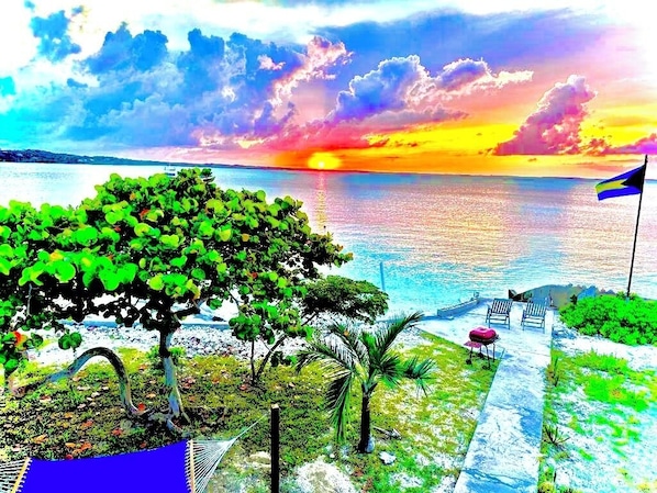 A beach view with a hammock, lounge chairs, and a flag.