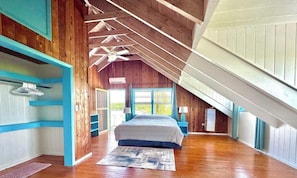 A bedroom with a sloped ceiling, wooden walls, a bed, and a large window.