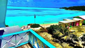 A beach view with a wooden deck, a flag, and a small building with a colorful roof. - Cottage style living directly on the Ocean (Georgetown)