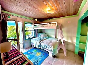 Una habitación con literas, una ventana con cortinas, una mesita con lámpara y una alfombra colorida.
