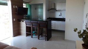 Een moderne keuken met een centraal eiland, een eethoek met stoelen en een aan de muur bevestigde televisie.