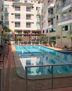 Una piscina con sillas de descanso y una zona de bar, rodeada de edificios de varios pisos con balcones.