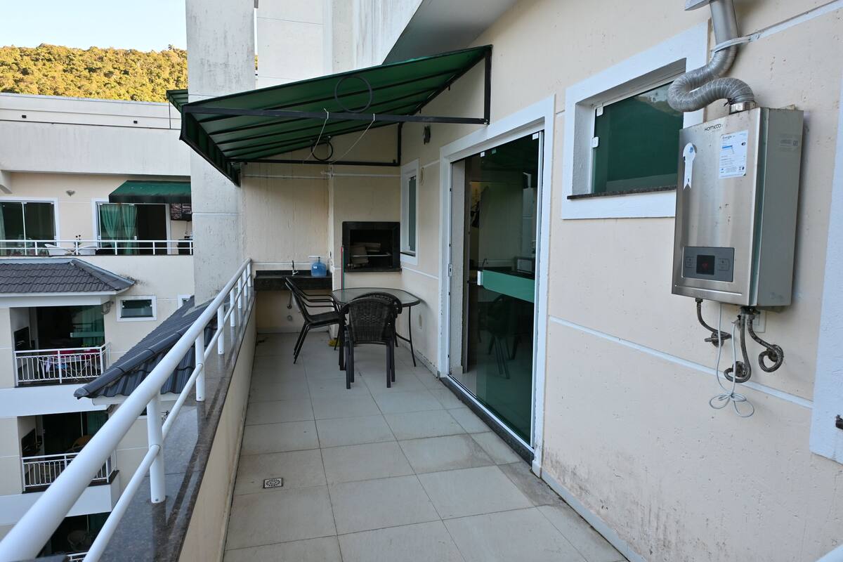 A balcony with a table and chairs, a green awning, and a utility box on the wall.
