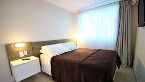 Een hotelkamer met een bed, nachtkastje, lamp en gordijnen.