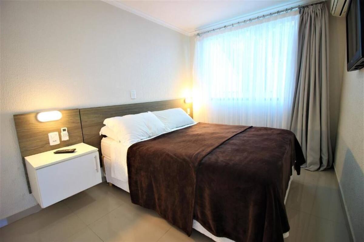 A hotel room with a bed, bedside table, lamp, and curtains.
