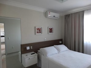 Una habitación de hotel con cama, mesitas de noche, aire acondicionado y cortinas.