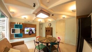 Een moderne woonkamer met een ronde eettafel, kleurrijke stoelen, een bank en een flatscreen televisie aan de muur.