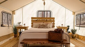 A tented room with a wooden bed, a bedside table, a lamp, and a window.