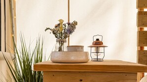 A wooden table with a Jackery Explorer 1000 portable power station underneath, a vase with flowers, a candle, and a lantern on top.