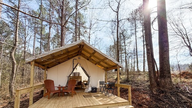 A wooden cabin with a covered porch, a dining table, and two Adirondack chairs.