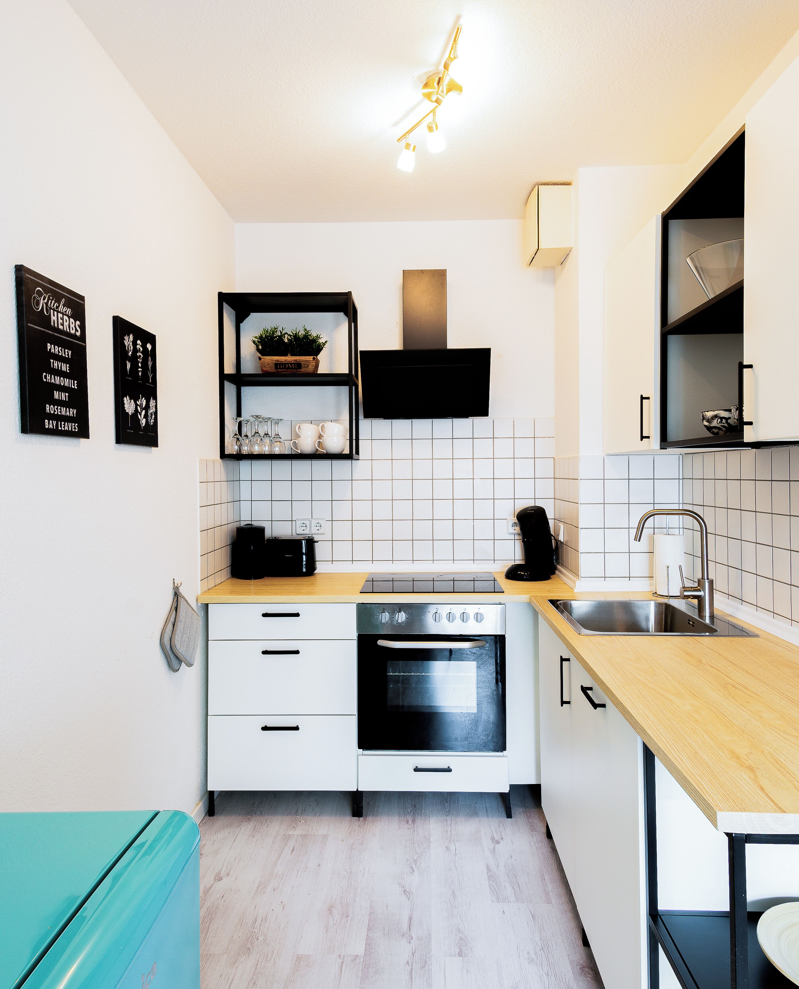 Eine moderne Küche mit weißen Schränken, einer Holz Arbeitsplatte, einem eingebauten Backofen und einer schwarzen Dunstabzugshaube. An der Wand befinden sich zwei schwarze Schilder und eine Deckenleuchte.