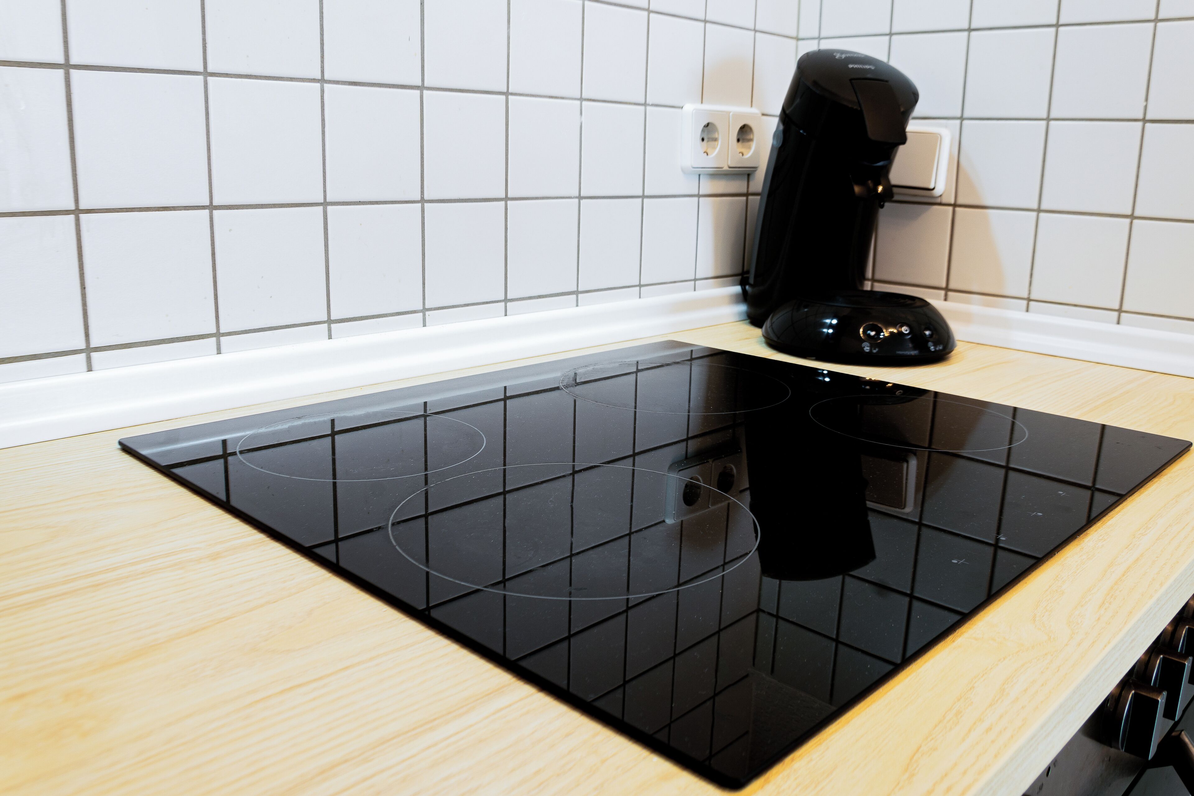 Una cocina moderna con una placa de inducción negra y una cafetera sobre la encimera.