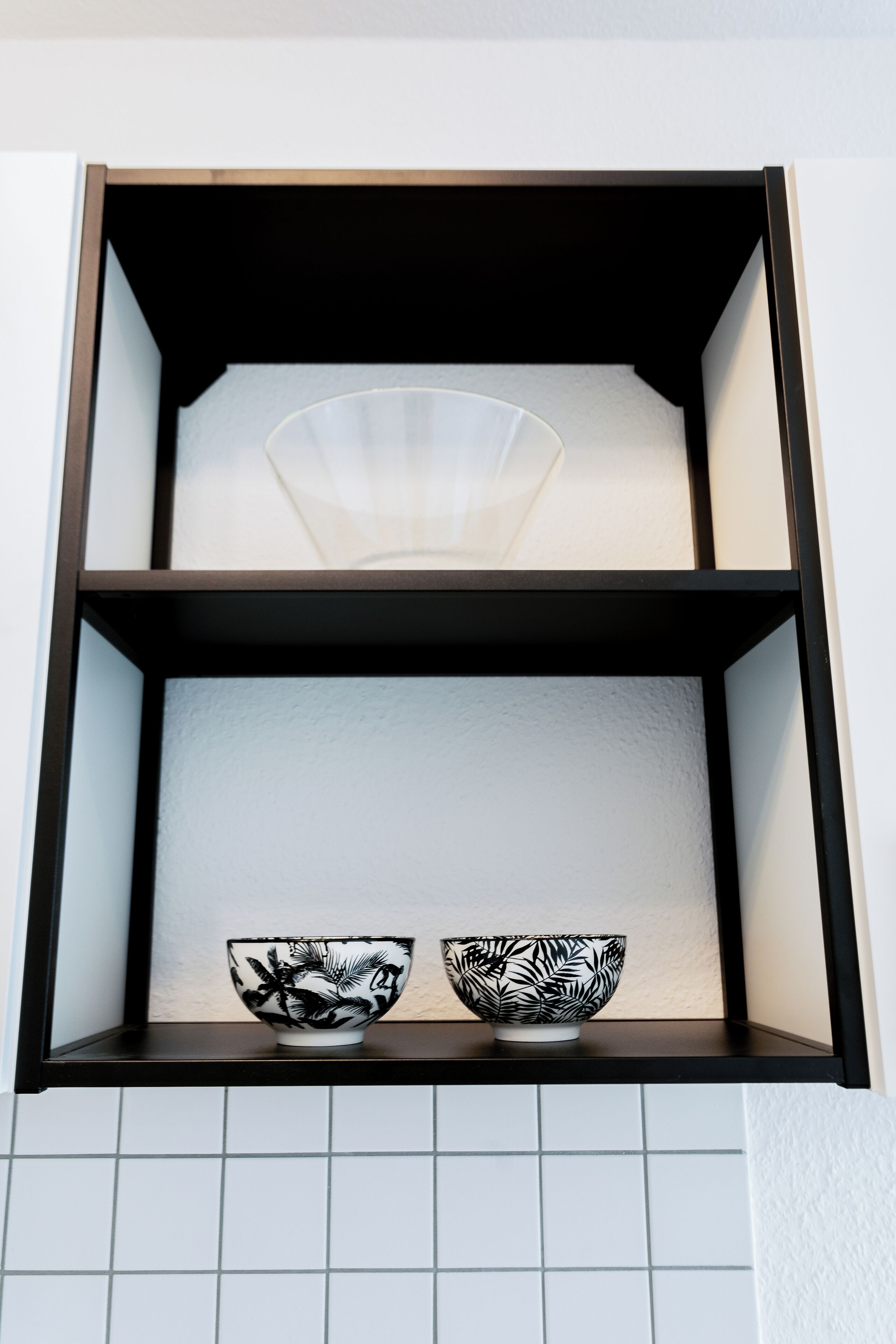 Ein Regal mit zwei schwarz-weiß gemusterten Schalen und einer transparenten Glaskugel.