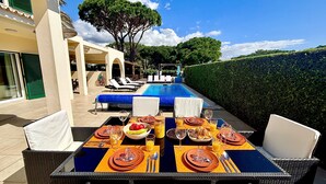 Een terras met eettafel, klaar voor een maaltijd, met uitzicht op een zwembad en rieten stoelen.