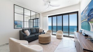 Ein modernes Wohnzimmer mit einem großen Fenster und Meerblick, einem Deckenventilator und einem großen Gemälde an der Wand.