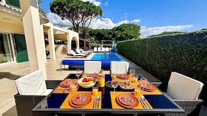 Een terras met eettafel, klaar voor een maaltijd, met uitzicht op een zwembad en rieten stoelen.