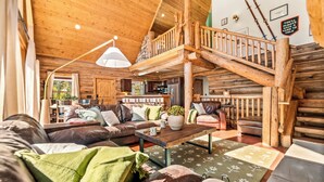 A log cabin interior with a wooden staircase, leather furniture, and a kitchen area. - Cozy Cabin • Hot Tub • Mtn Views • Firepit • Near Breck (Fairplay)