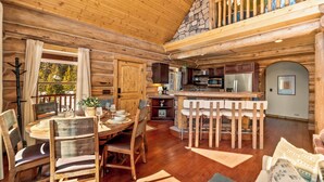 A log cabin interior with a dining area, kitchen, and a stone fireplace. - Cozy Cabin • Hot Tub • Mtn Views • Firepit • Near Breck (Fairplay)