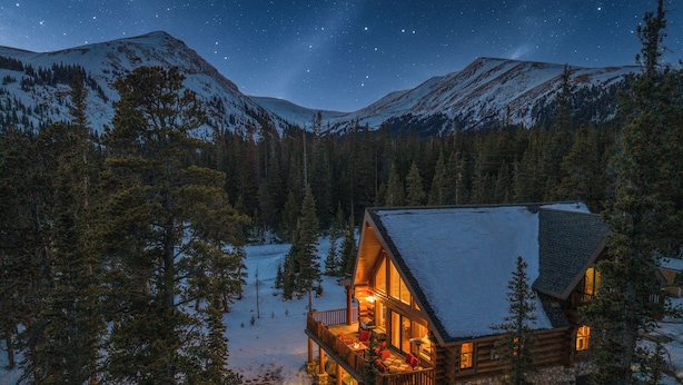 A log cabin with a deck, surrounded by snow-covered mountains and trees. - Cozy Cabin • Hot Tub • Mtn Views • Firepit • Near Breck (Fairplay)