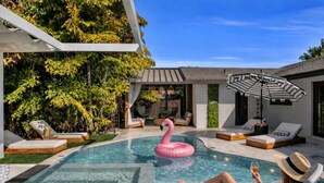 En swimmingpool med liggestole, en lyserød flamingo-svømmelegetøj, og en person der slapper af med en drink.