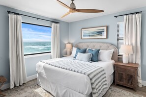 Ein Schlafzimmer mit einem großen Bett, einem Deckenventilator, Meerblick und einem Nachttisch mit Lampe.
