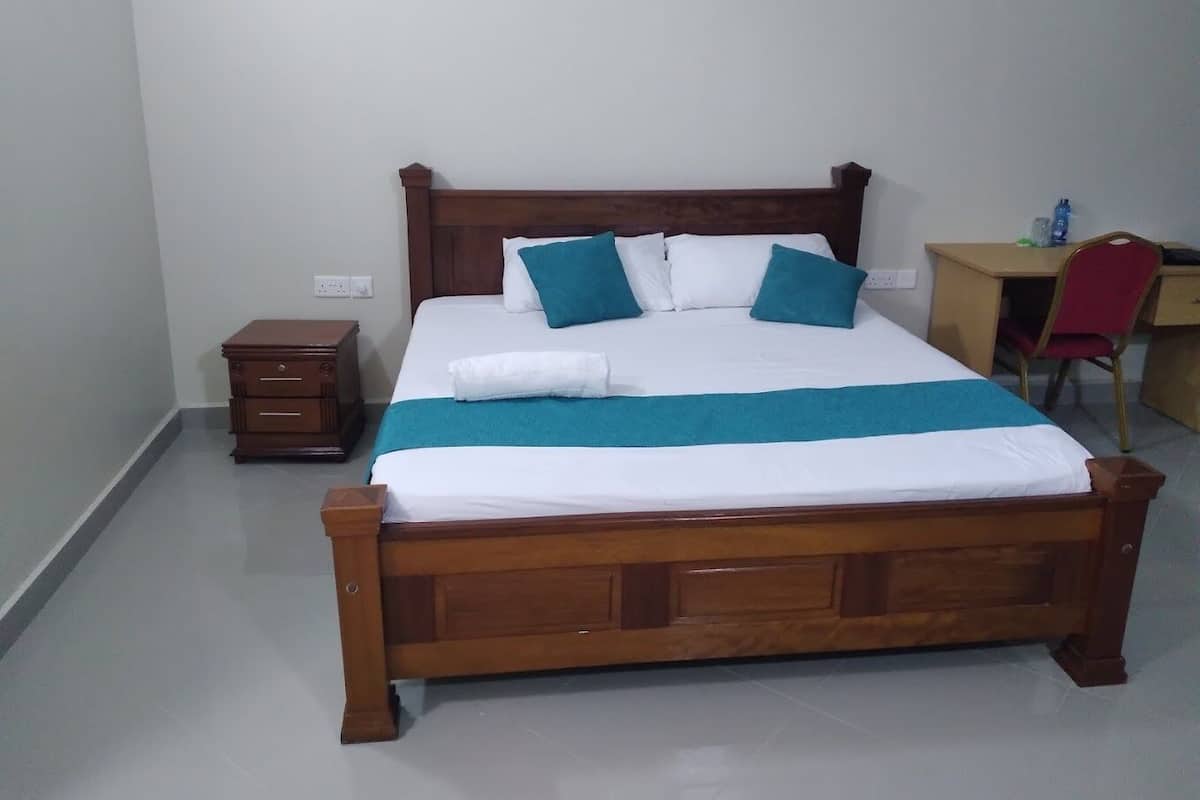 A neatly made bed with a wooden frame, a small bedside table, and a desk with a chair.