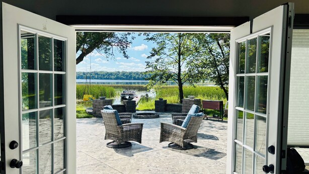 An open patio with wicker chairs and a fire pit, overlooking a lake and boats.
