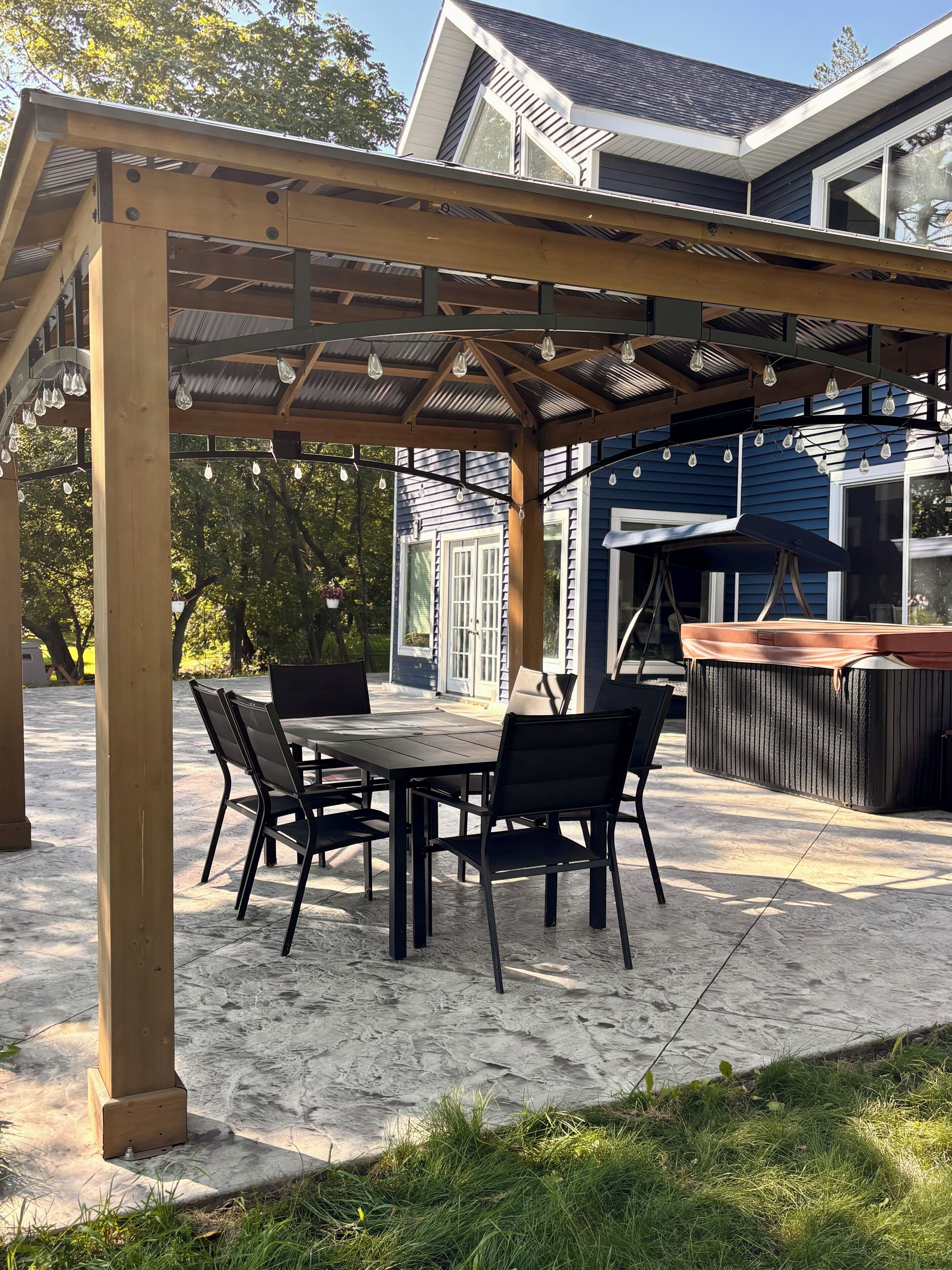 Un patio couvert comprenant une table et des chaises, un barbecue et une structure en forme de pergola.