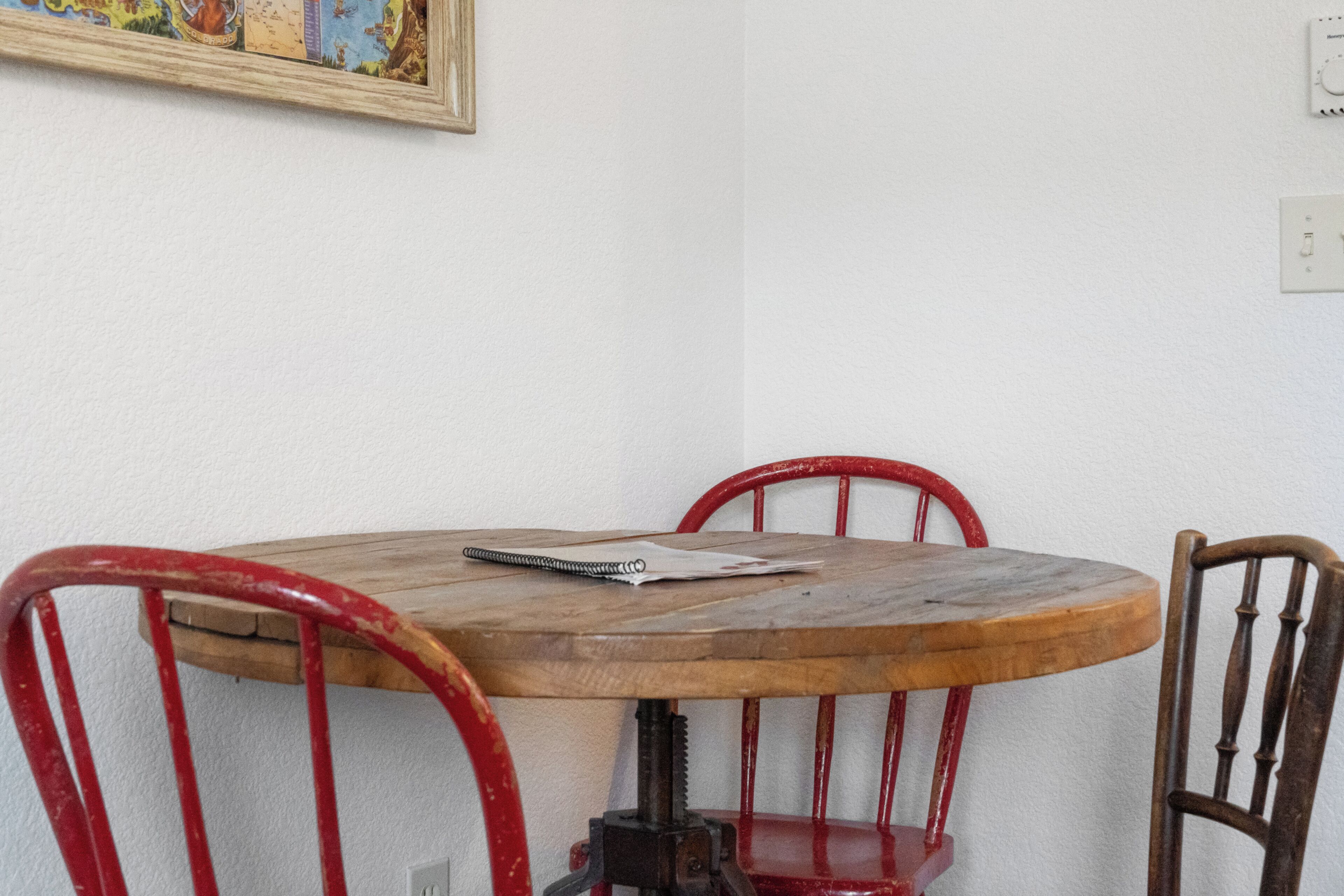 Una pequeña mesa de madera con un cuaderno y un bolígrafo, rodeada de sillas rojas.