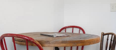 Una pequeña mesa de madera con un cuaderno y un bolígrafo, rodeada de sillas rojas.
