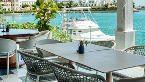 An outdoor patio with a view of the sea, featuring a table and chairs, a potted plant, and a yacht in the background. - Stylish Cap Cana Apartment • Pool, Gym & Beaches (Punta Cana)